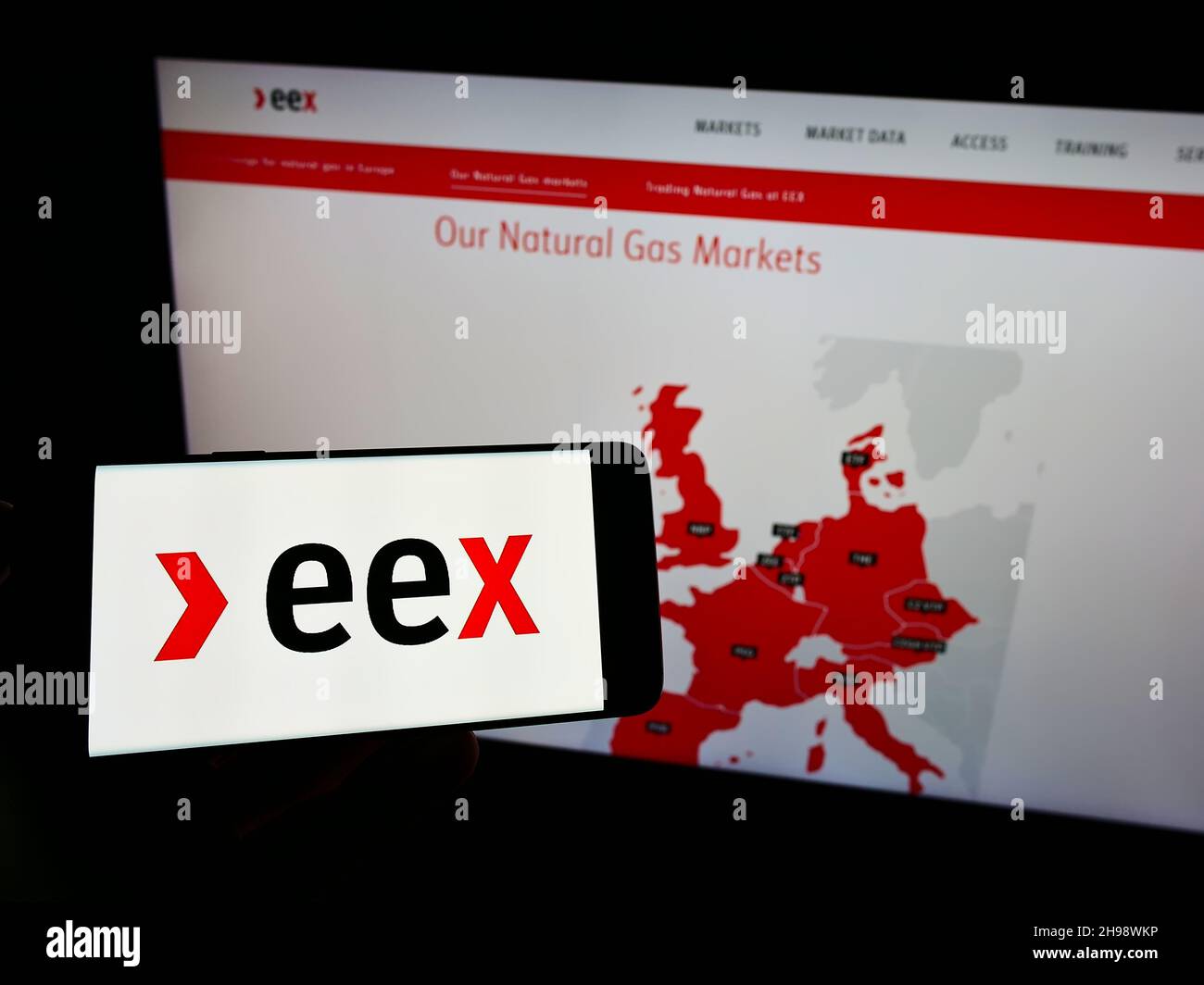 Person holding smartphone with logo of German company European Energy Exchange AG (EEX) on screen in front of website. Focus on phone display. Stock Photo