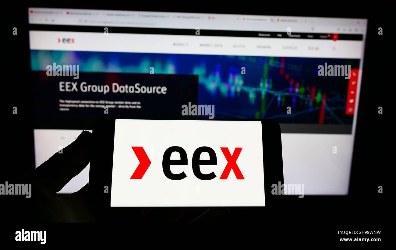 Person holding cellphone with logo of German company European Energy Exchange AG (EEX) on screen in front of webpage. Focus on phone display. Stock Photo