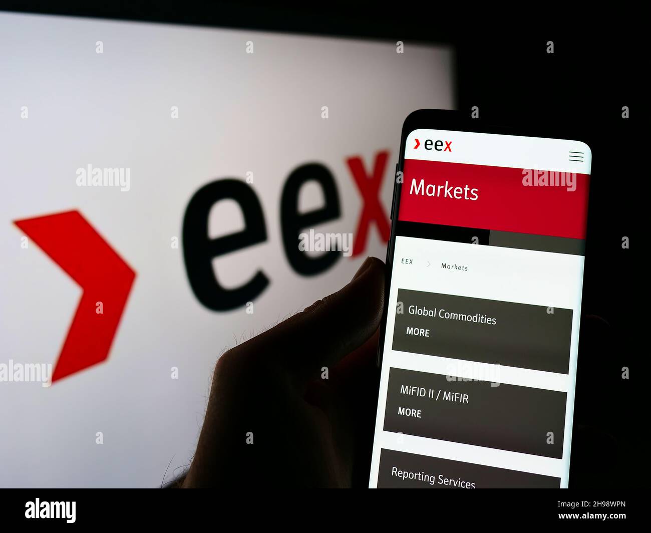Person holding cellphone with webpage of German company European Energy Exchange AG (EEX) on screen with logo. Focus on center of phone display. Stock Photo