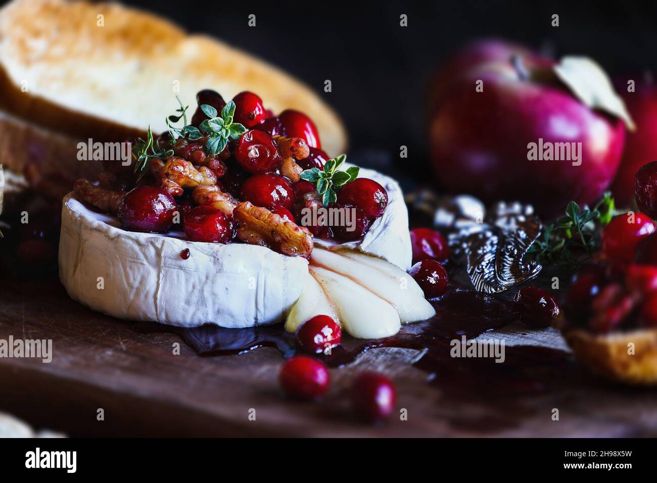 Baked Camembert Brie cheese with a cranberry, honey, balsamic vinegar and nut relish and garnished with thyme. Served with toasted bread slices and ap Stock Photo