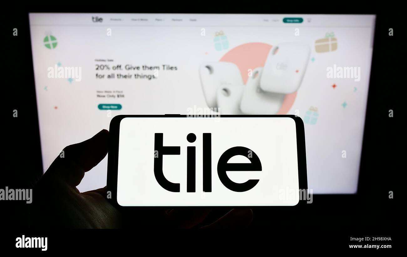 Person holding smartphone with logo of US consumer electronics company Tile Inc. on screen in front of website. Focus on phone display. Stock Photo