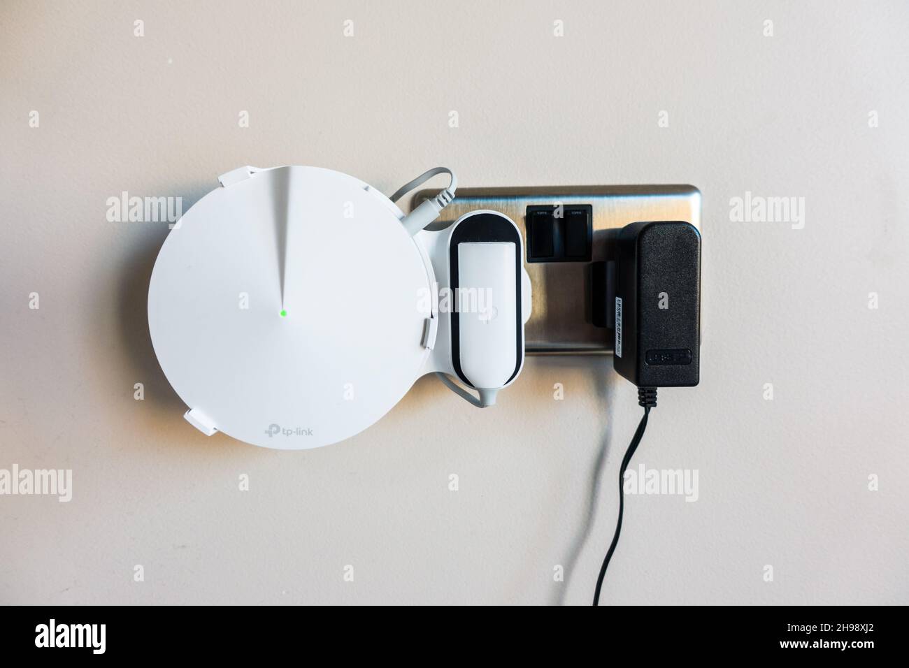 Whole Home WiFi systems / WiFi Mesh device tucked into a holder next to plug point Stock Photo