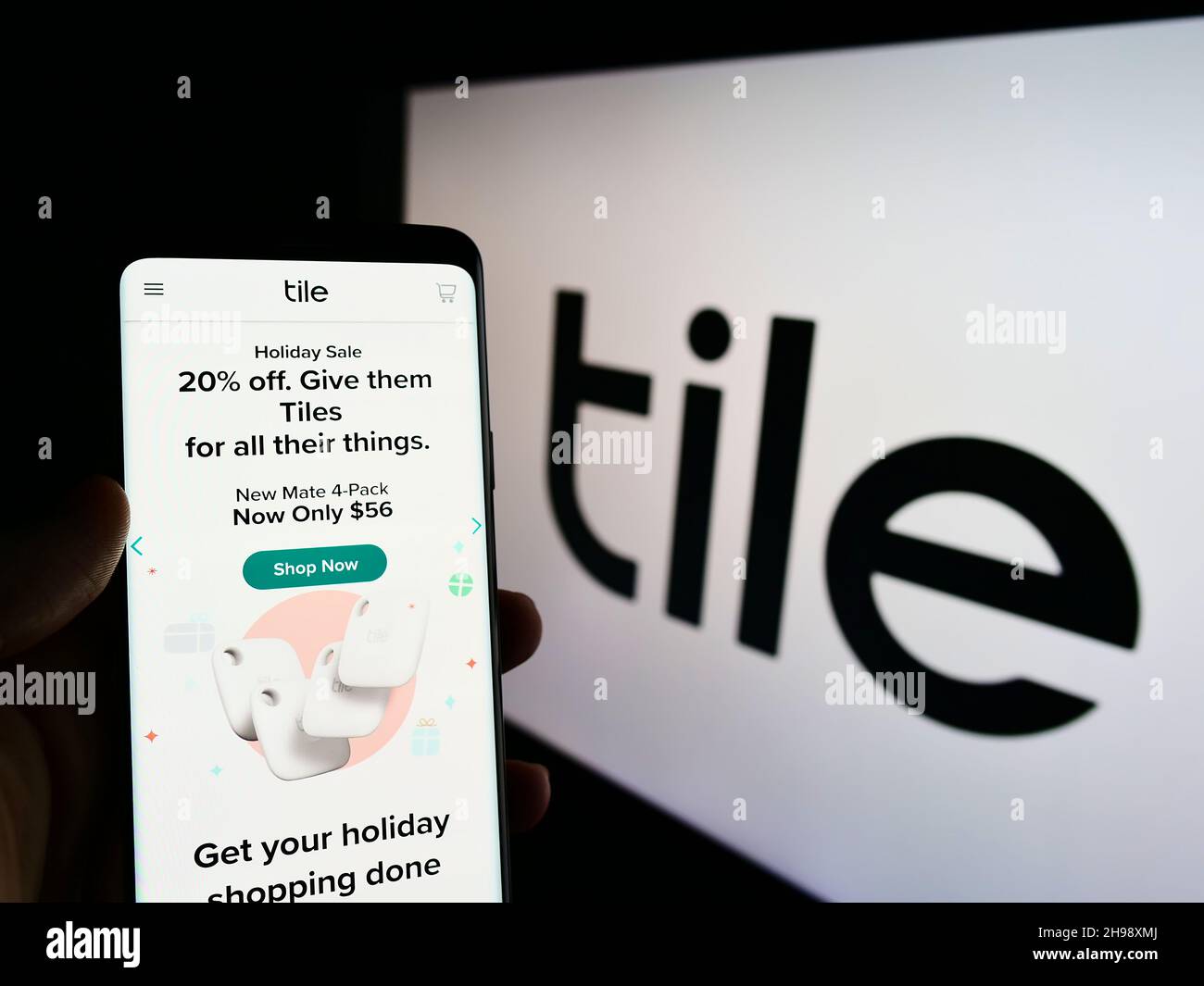 Person holding cellphone with website of US consumer electronics company Tile Inc. on screen in front of logo. Focus on center of phone display. Stock Photo