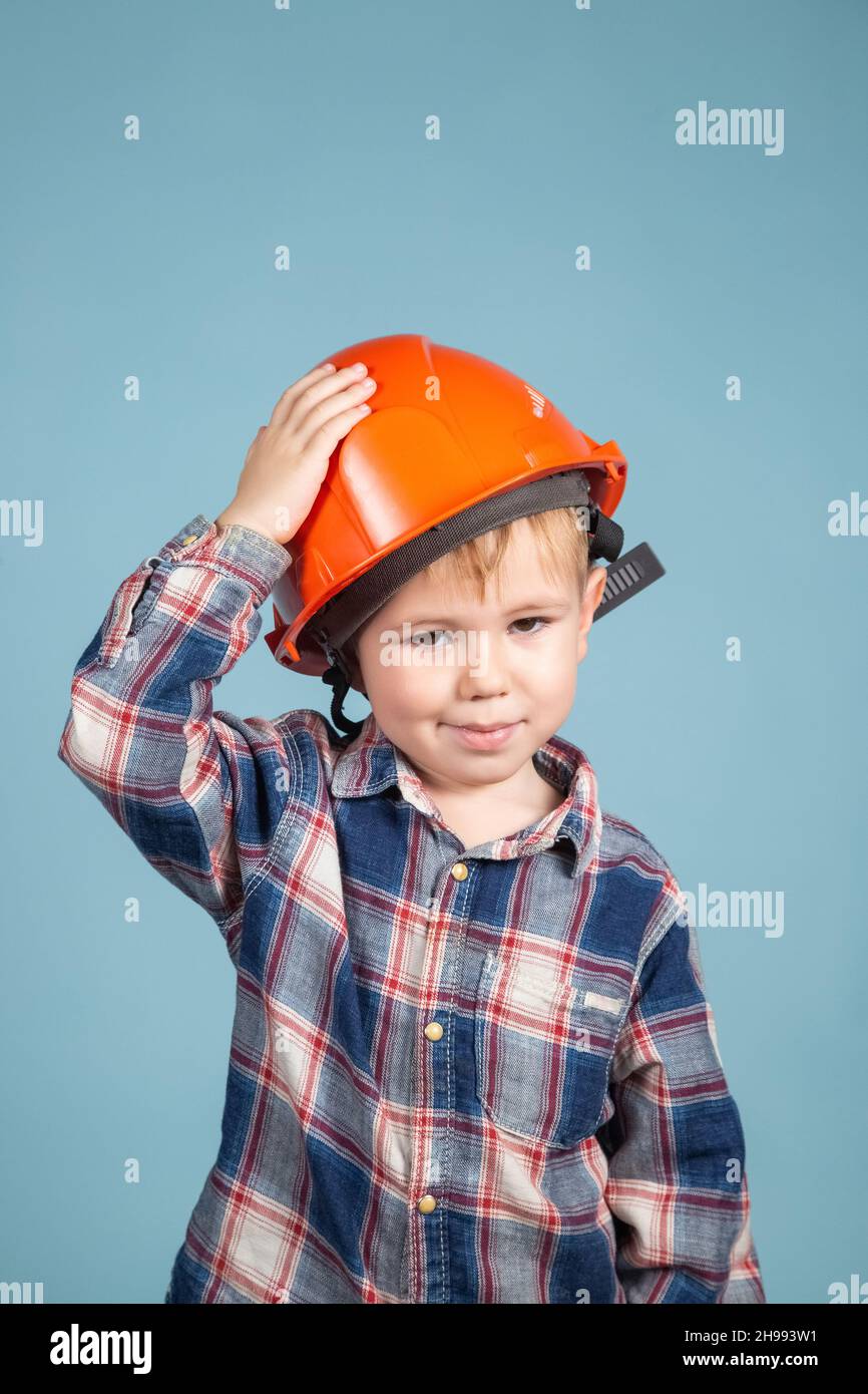 Portrait of cute little boy in a protective orange helmet over blue background. Concept of Construction and repair. Stock Photo