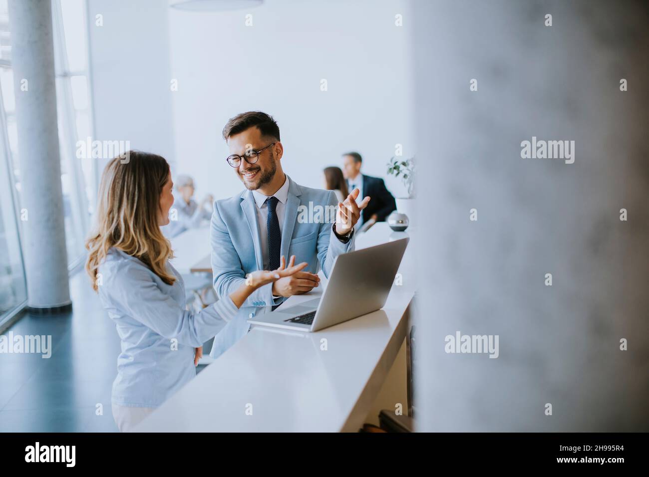 Young business couple working and discussing by laptop in the office in front of their team Stock Photo