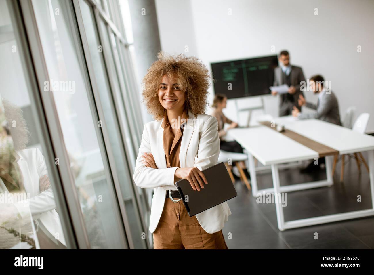 Young curly hair businesswoman using digital tablet in the office with young people works behind her Stock Photo