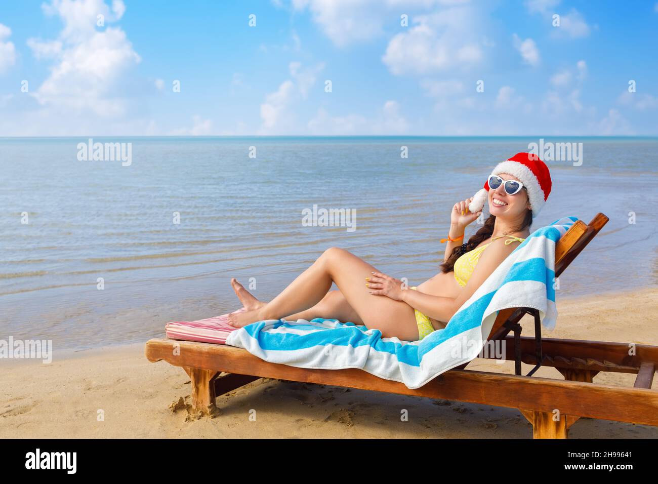 cheerful young woman in santa hat and sunglasses lying on sun lounger Stock Photo