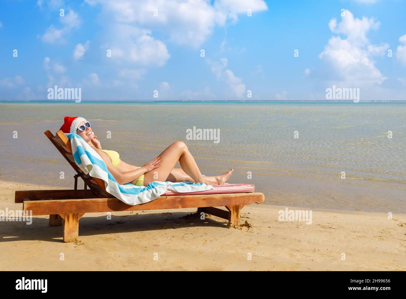 young woman in santa hat and sunglasses relaxing on sun lounger Stock Photo