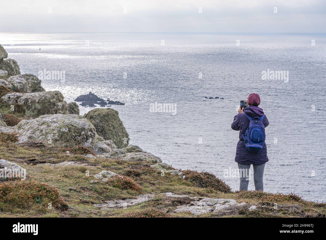 A typical rugged piece of Cornish coastline with a lady taking a photograph with a mobile phone of the stunning views. Stock Photo