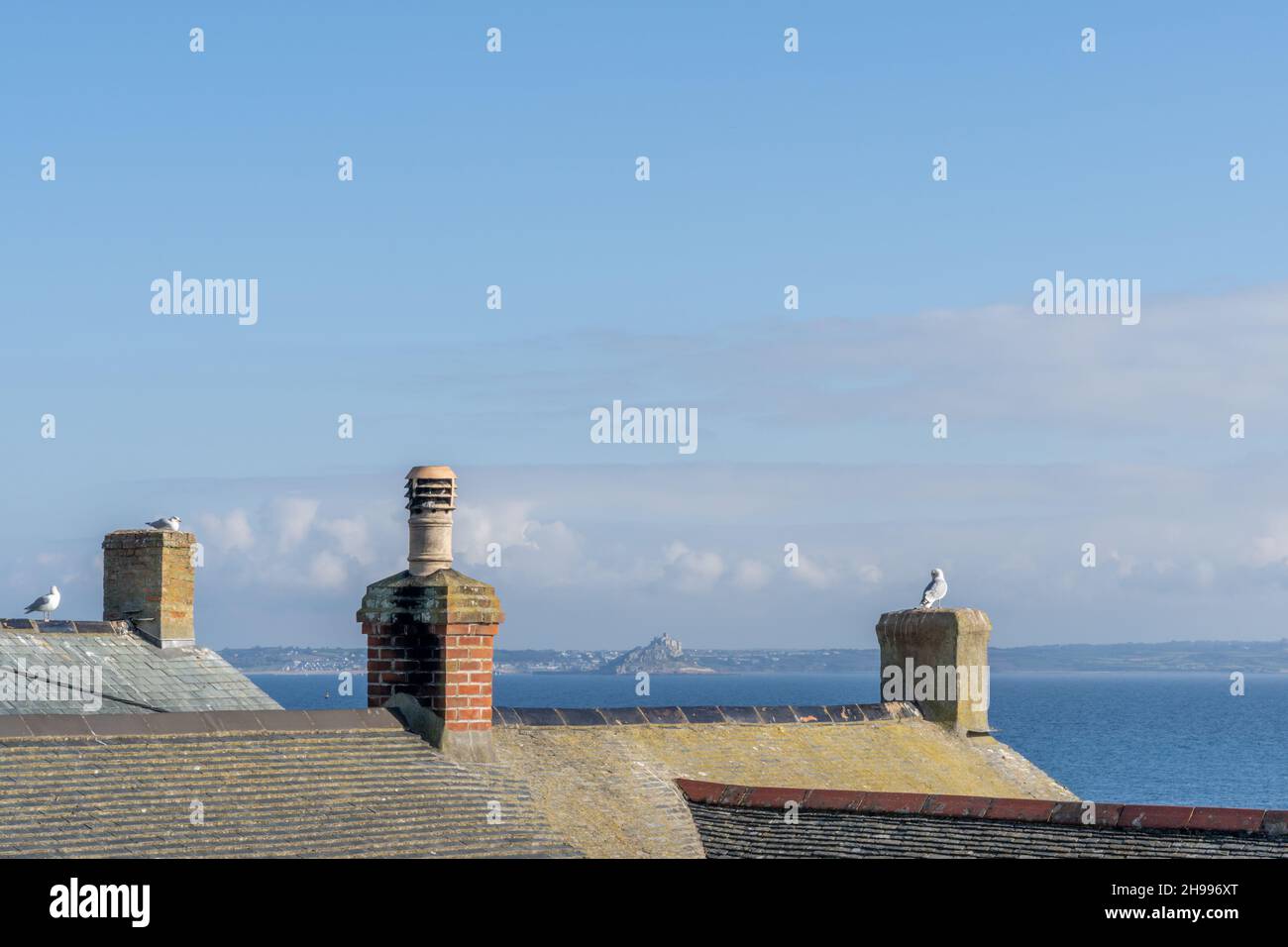 The rooftops of Mousehole with resting gulls and far reaching views towards St Michael's Mount in Cornwall Stock Photo