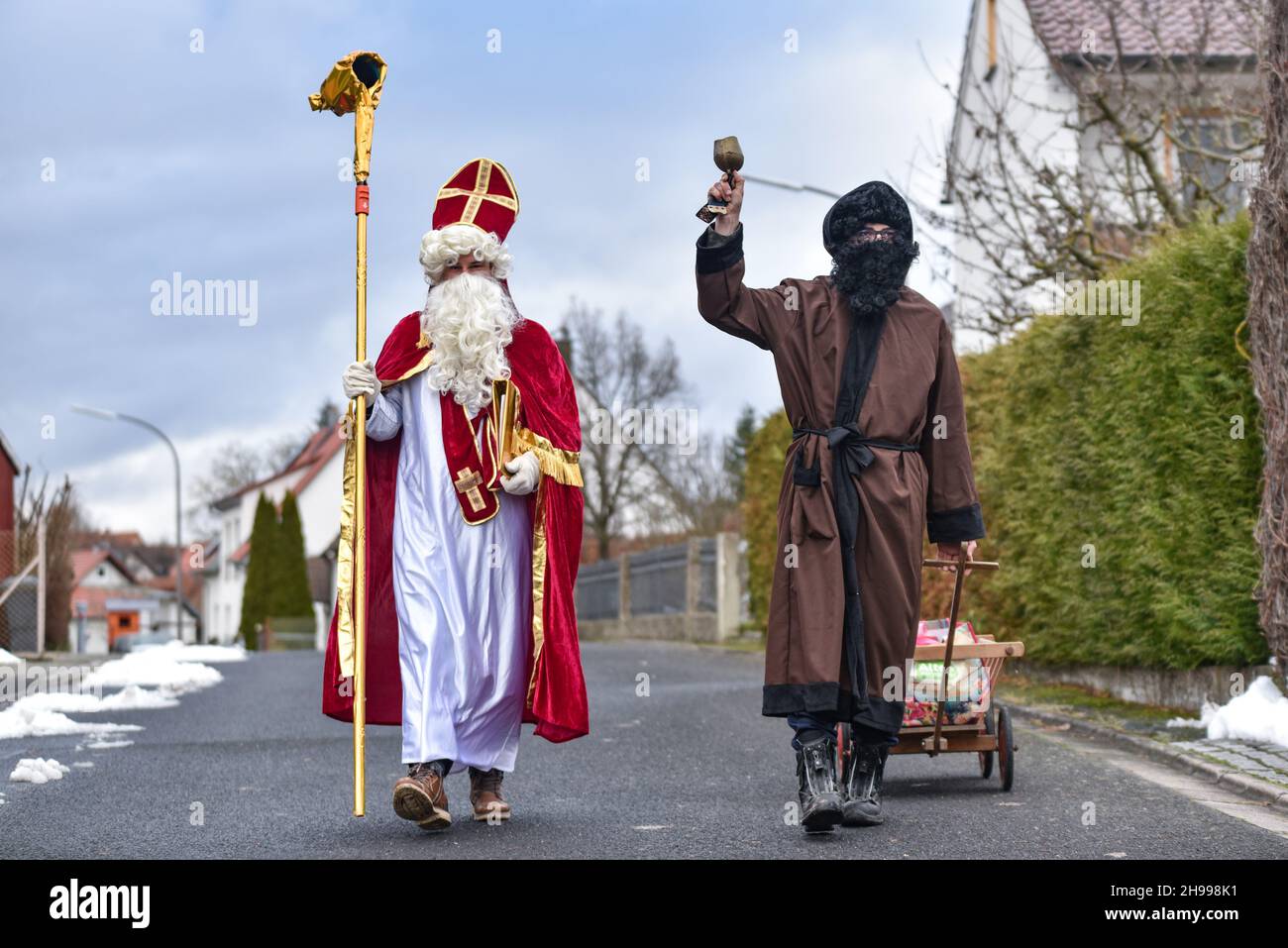 Germany ,Kirchlauter,  - 05 Dec 2021 - Local News - St. Nikolaus fundraiser for Franken Hospice Bamberg    Image: Markus Geier (Nikolaus) and Jan Schneiderbanger (Knecht Ruprecht) walk around the town of Kirchlauter, dressed as the Christmas pair, delivering goodies to children along a registered route. Those taking part donate money, 100% of the money is sent to a youth hospice in Bamberg, Germany. Stock Photo