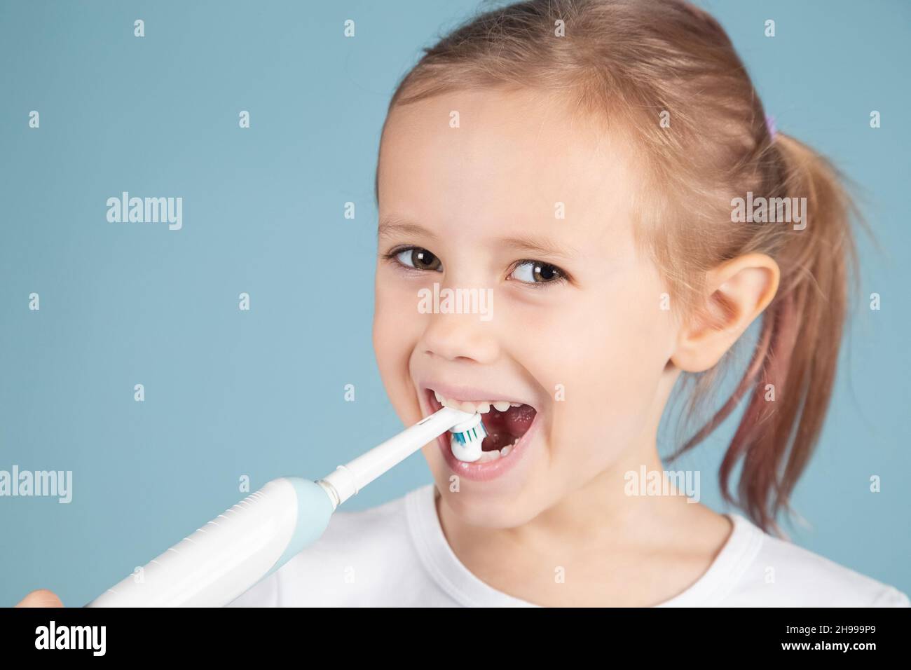 Portrait of cute little caucasian girl brushing teeth Standing Over blue Background, hygiene concept Stock Photo
