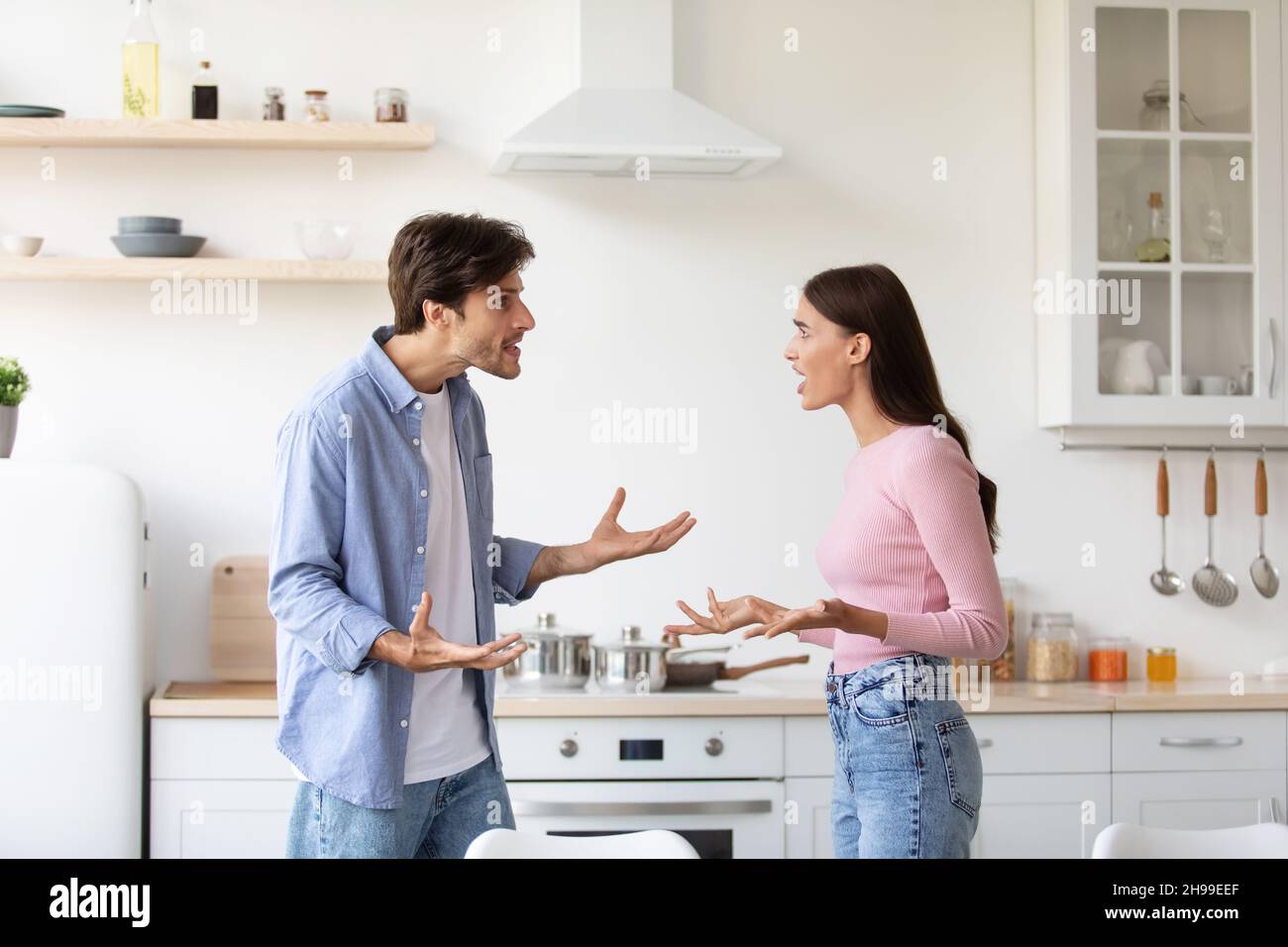 Angry offended young wife and husband shout, swear in kitchen interior. Couple arguing and conflicting Stock Photo