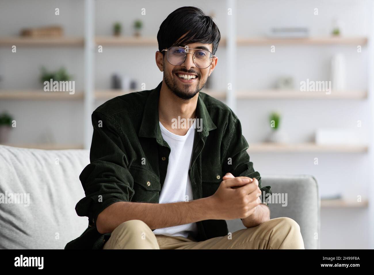 Positive middle eastern guy sitting on couch at home Stock Photo