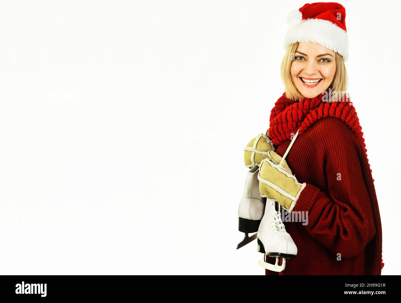 Smiling woman with ice skates. Beautiful girl in Santa hat with figure skates. Winter sport activity. Copy space Stock Photo