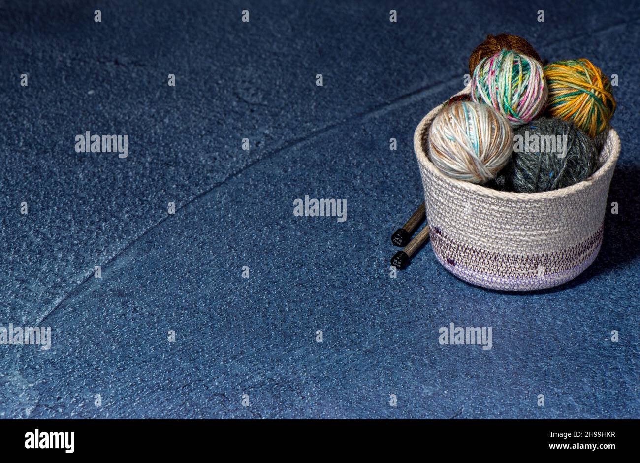 Skeins of yarn knitting needles in a beige fabric bowl and blue background Stock Photo