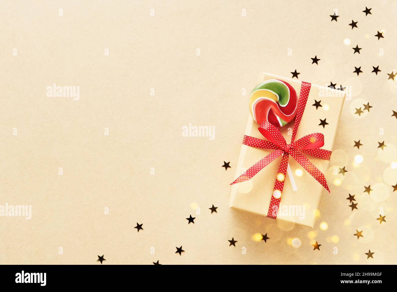 Christmas gift box decorated with red ribbon and colorful lollipop on a craft paper background. Top view, copy space for text Stock Photo