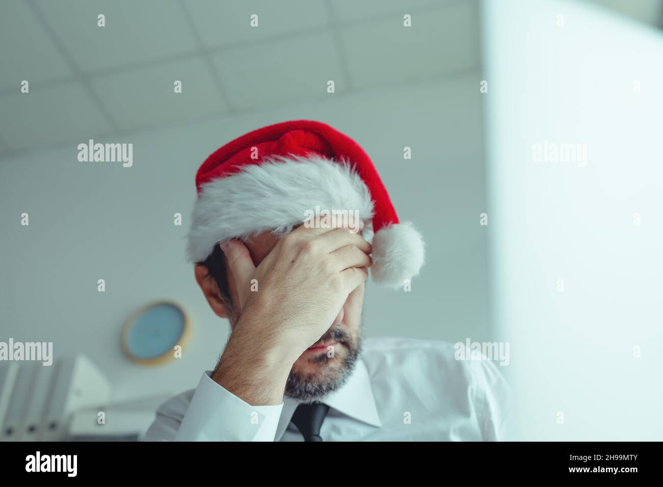 Disappointed businessman with Santa Claus hat suffering from Christmas holiday season depression in office, selective focus Stock Photo