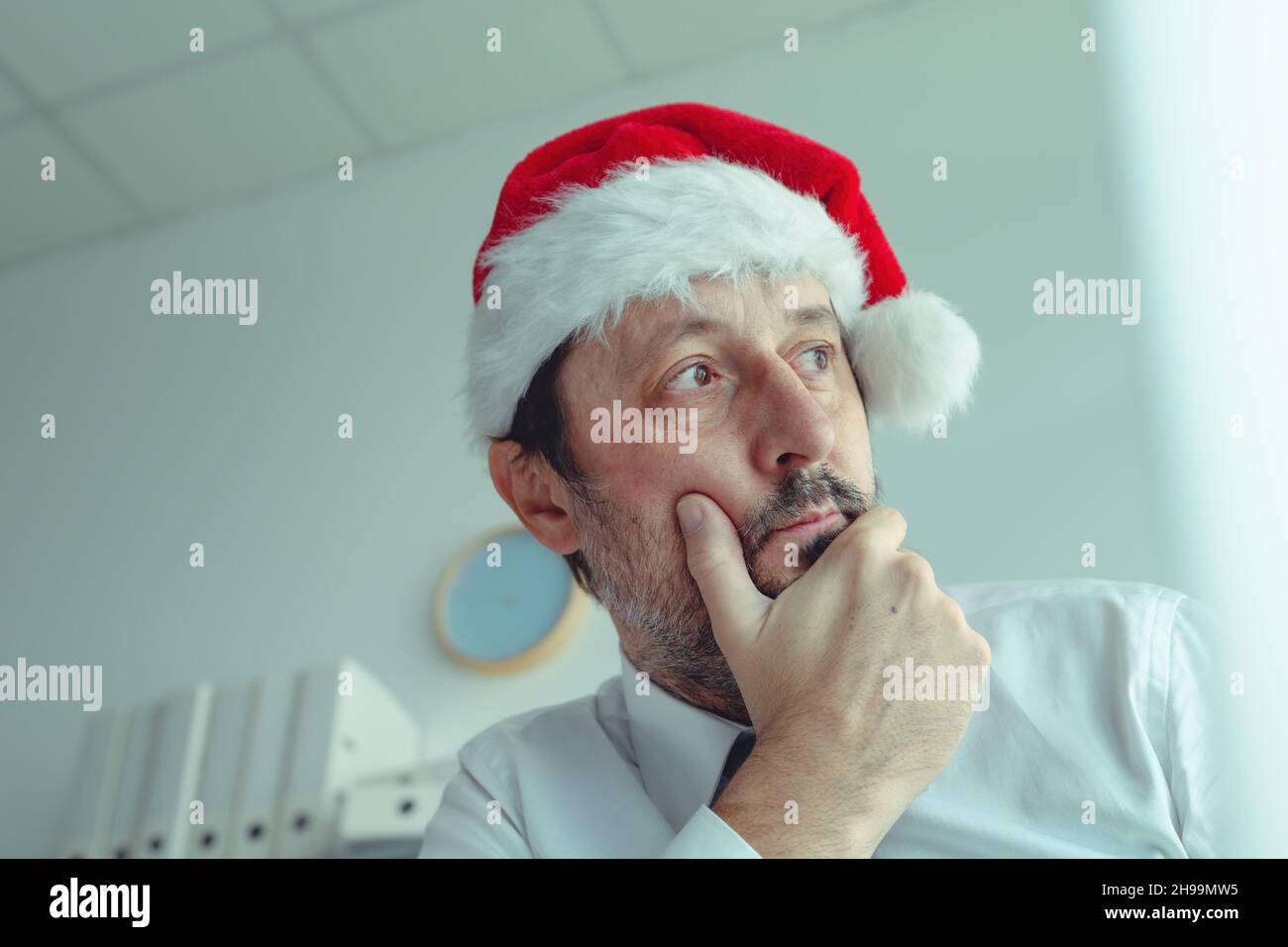 Melancholic businessman with Santa Claus hat suffering from Christmas holiday season depression in office, selective focus Stock Photo