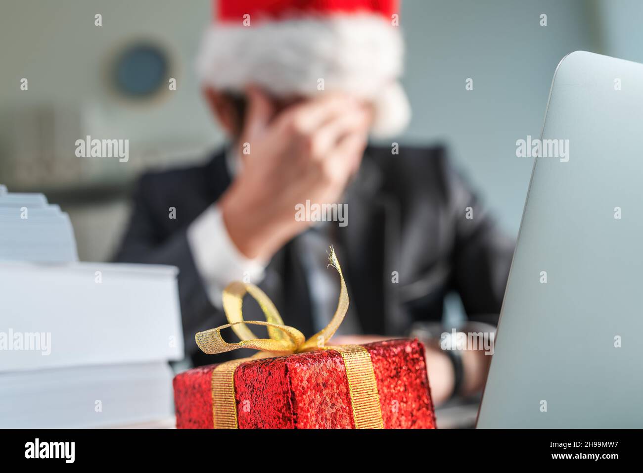 Sad and unhappy businessman with Santa Claus hat crying in office during Christmas holiday season, wrapped present on the desk with selective focus Stock Photo