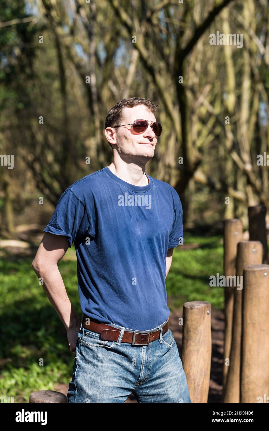Portrait of a man in a blue shirt and jeans standing in a  nature park Stock Photo