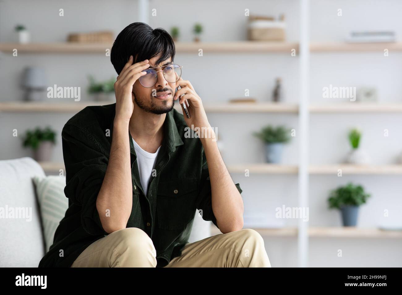 Upset indian guy having phone conversation, home interior Stock Photo