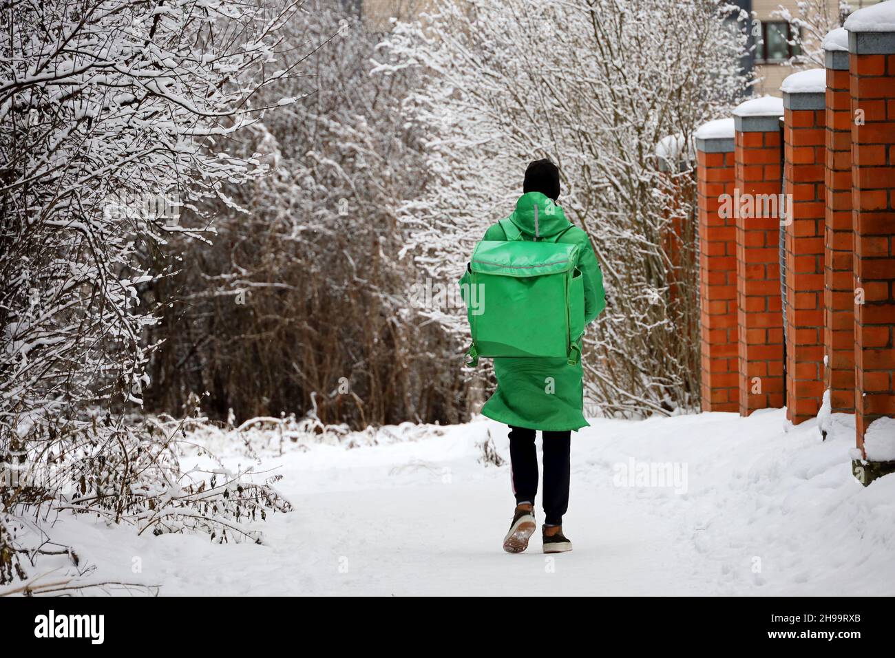 Delivery service courier with a thermos bag walking down the snow in winter city. Food delivery home Stock Photo