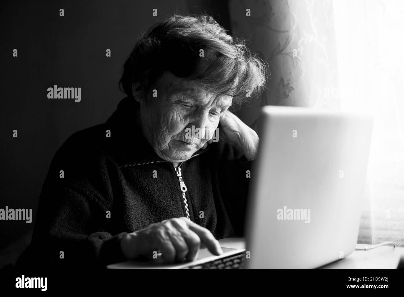 An old woman is learn to type  on a laptop in her home. Black and white photo. Stock Photo
