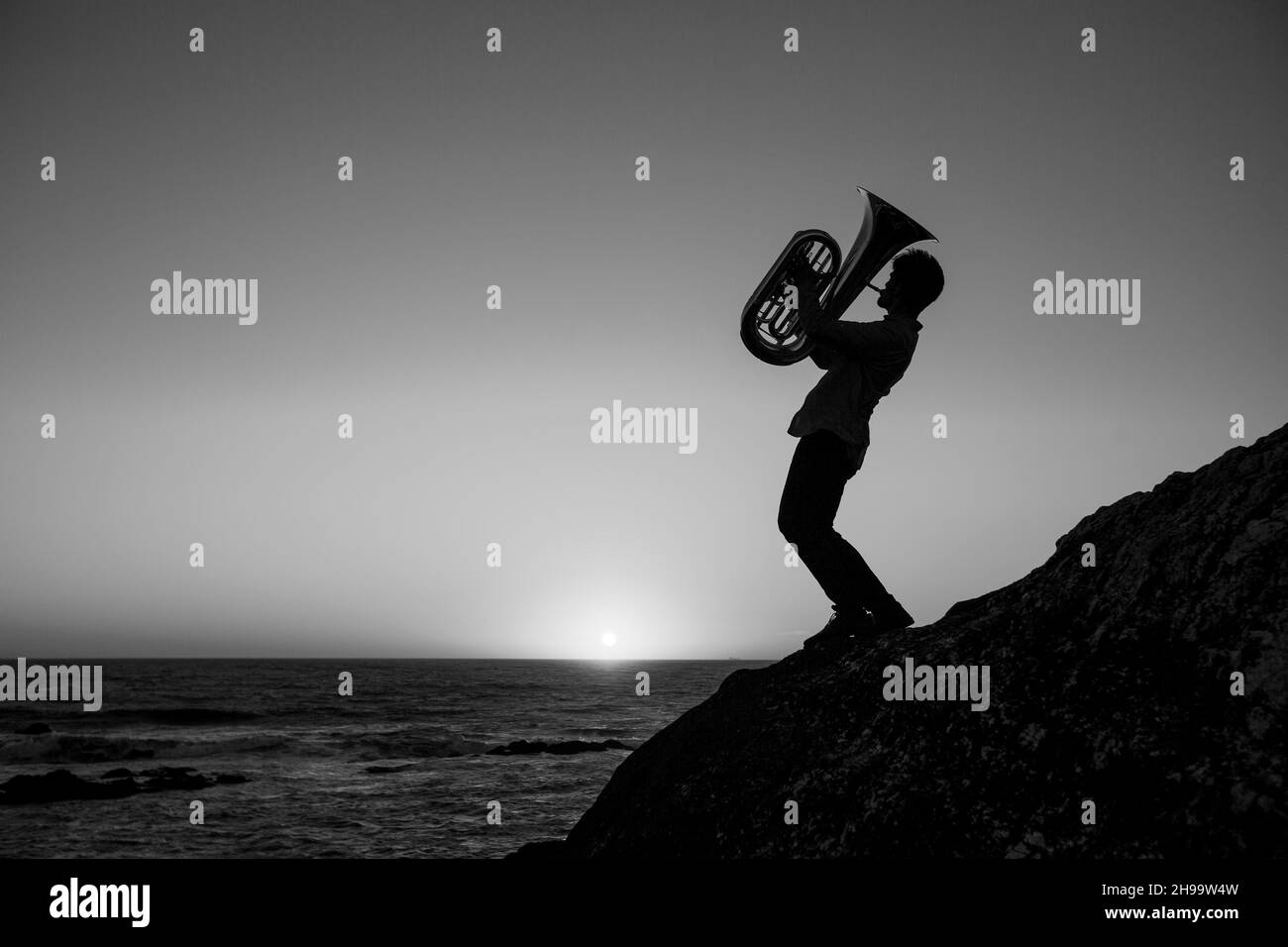 Silhouette of a man playing a trumpet by the ocean. Black and white photo. Stock Photo