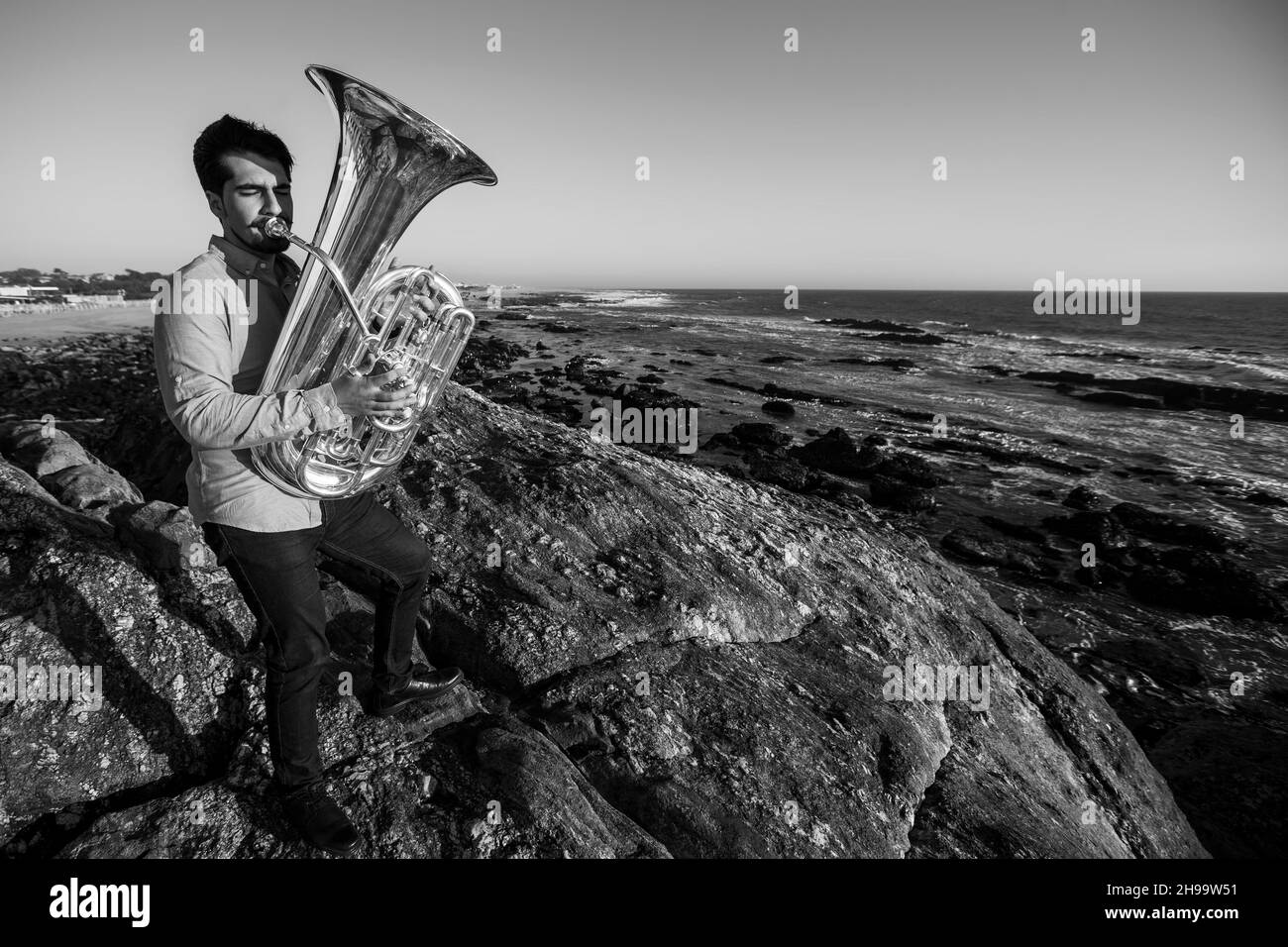 Musician standing on the rocks with a tuba on the ocean shore. Black and white photo. Stock Photo