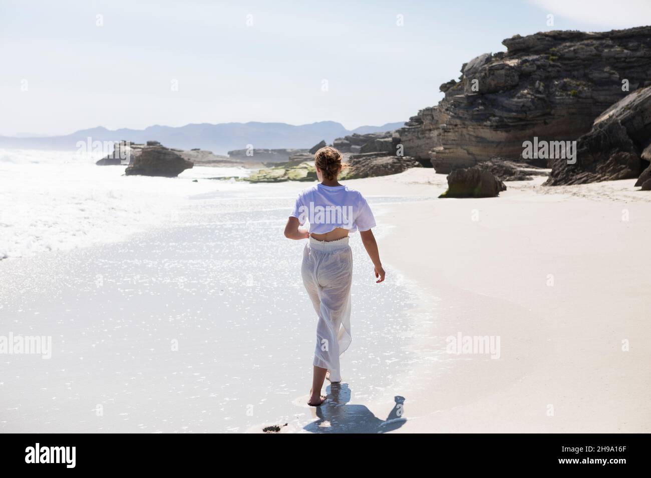 Teenage girl walking on a sandy beach at the water's edge Stock Photo