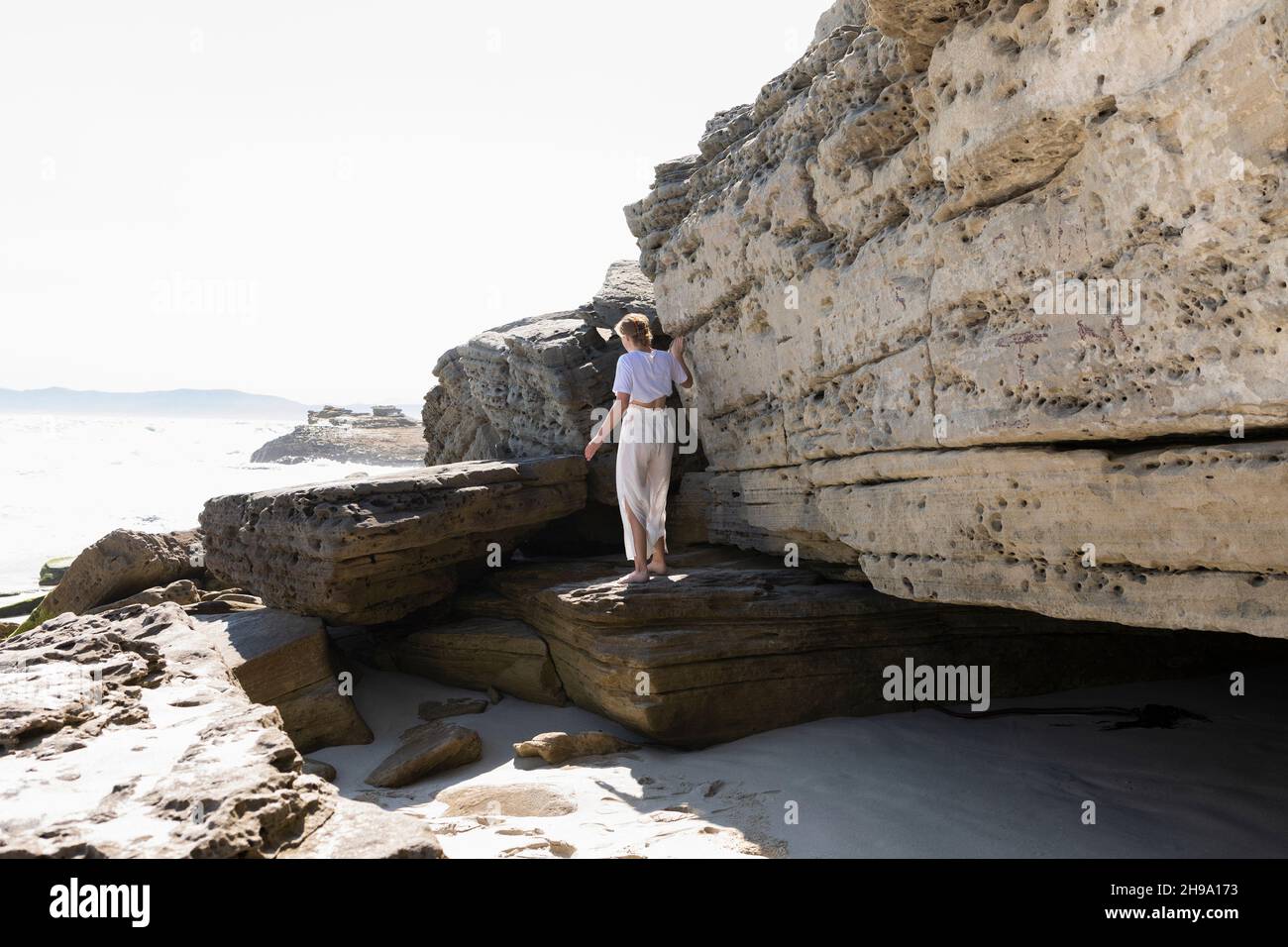 Teenage girl exploring the cliffs and rock strata on a beach on the Atlantic shore. Stock Photo