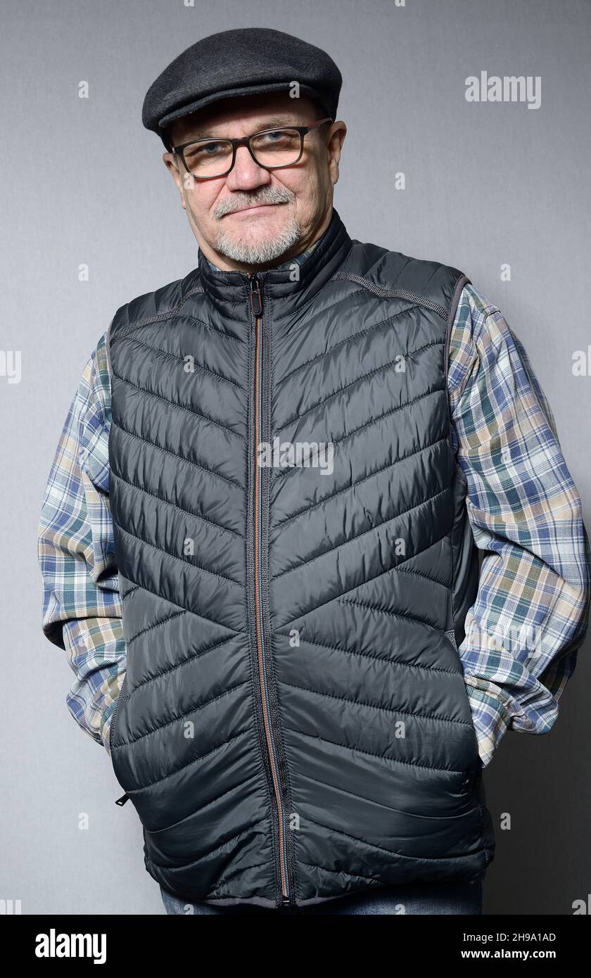 a senior man in a down vest with glasses and a cap on a neutral background, half length portrait Stock Photo