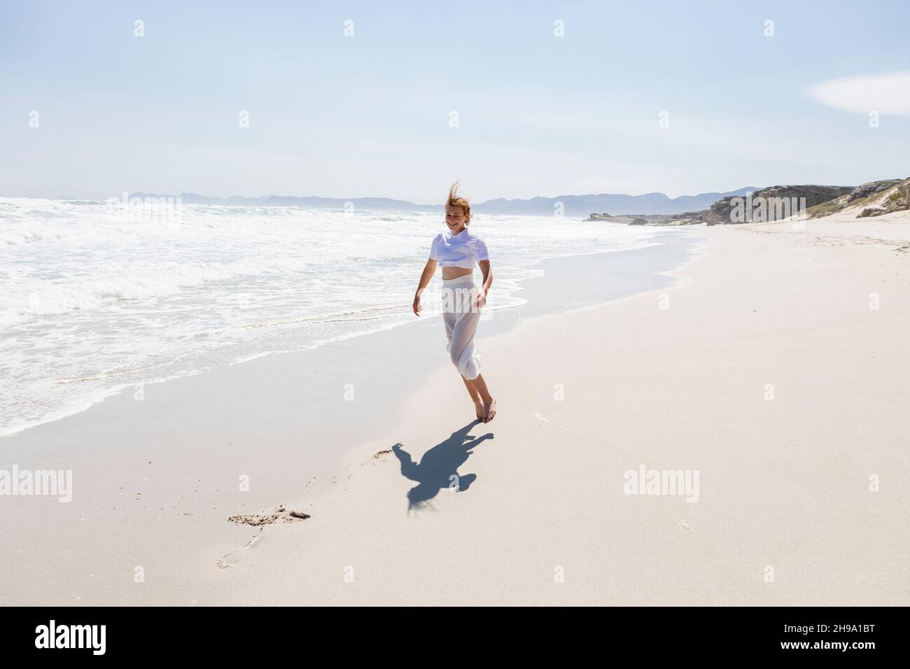 Teenage girl dancing alone on a sandy beach in South Africa by the water's edge Stock Photo