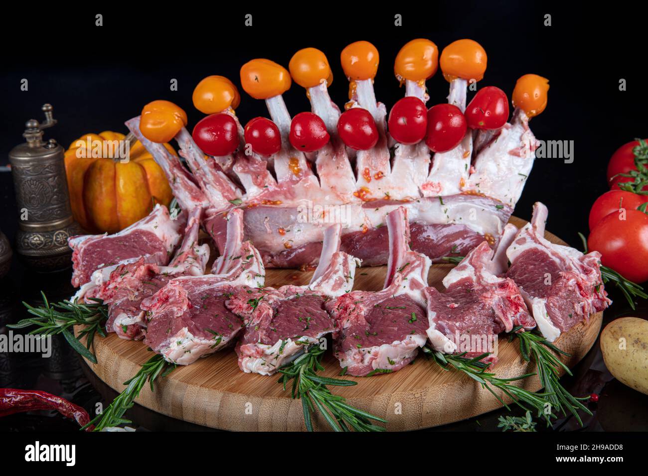 Raw fresh rack of lamb with green herbs. Racks of lamb ready for cooking on dark background. Raw ribs with a rosemary and vegetables. Stock Photo