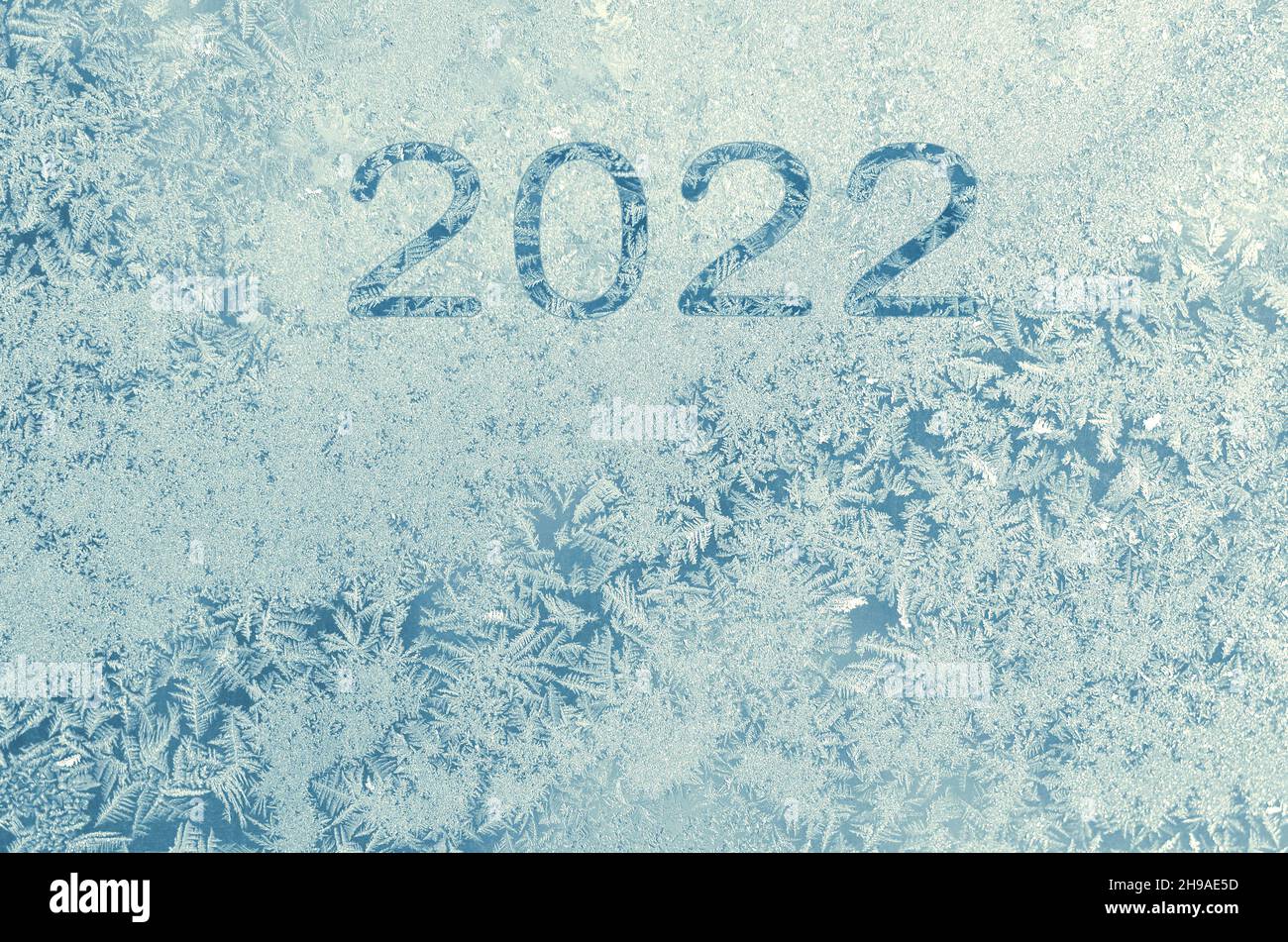 Inscription about the new year 2022 on the frosty patterns on the window glass in the winter season as a light blue background with copy space. Happy Stock Photo