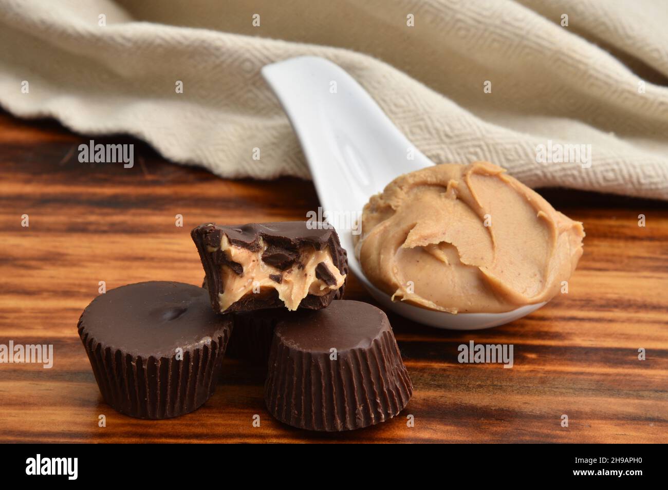 Dark chocolate peanut butter cups with a missing bite and a spoonful of creamy peanut butter on a dark wooden table Stock Photo