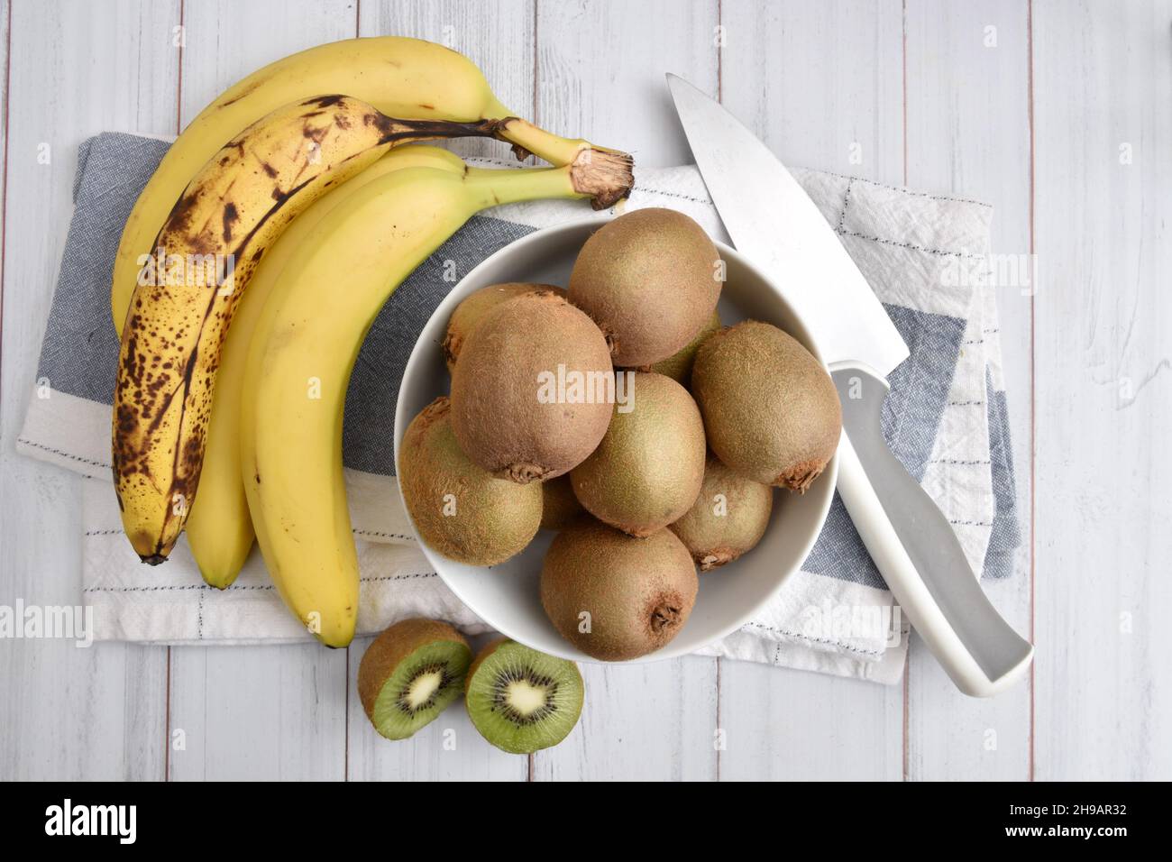 Overhead view of a bowl of kiwi fruit with bananas and apples on wooden table Stock Photo