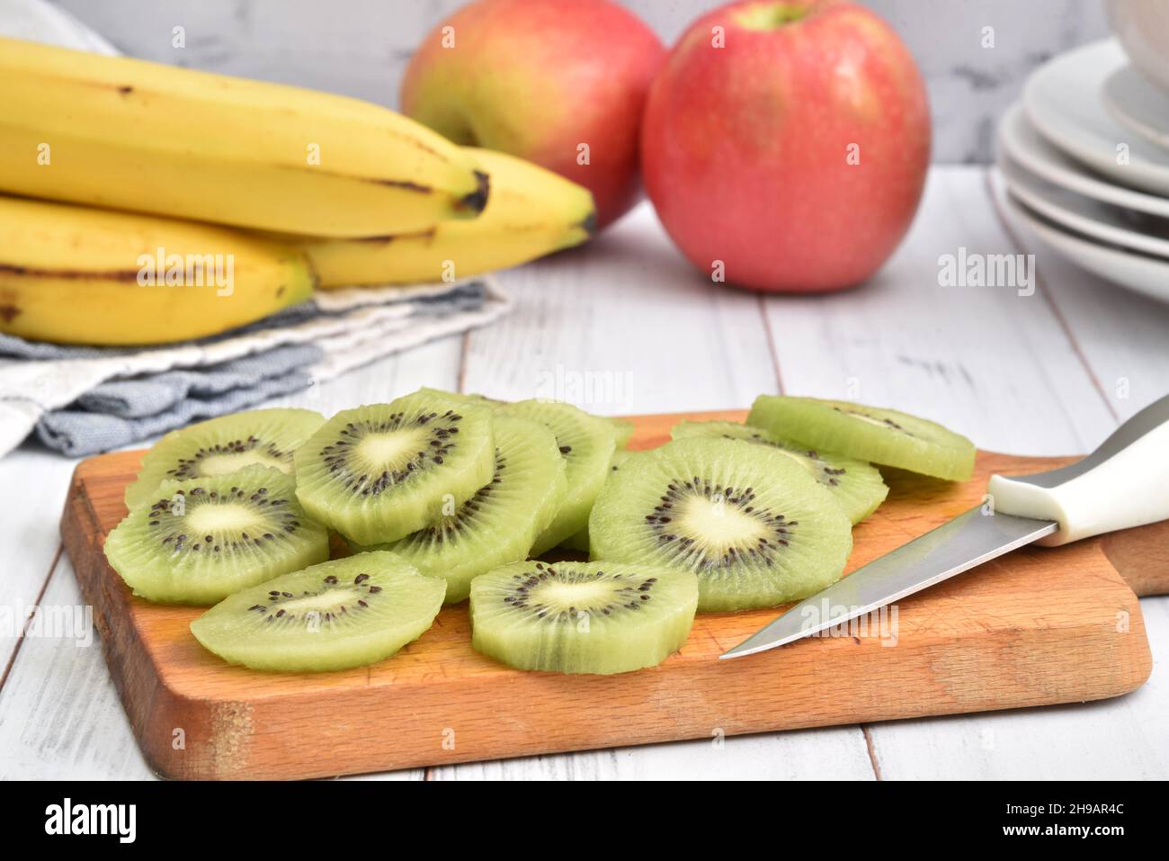 Kiwi slices on a cutting board with bannanas and apples on a wooden table Stock Photo