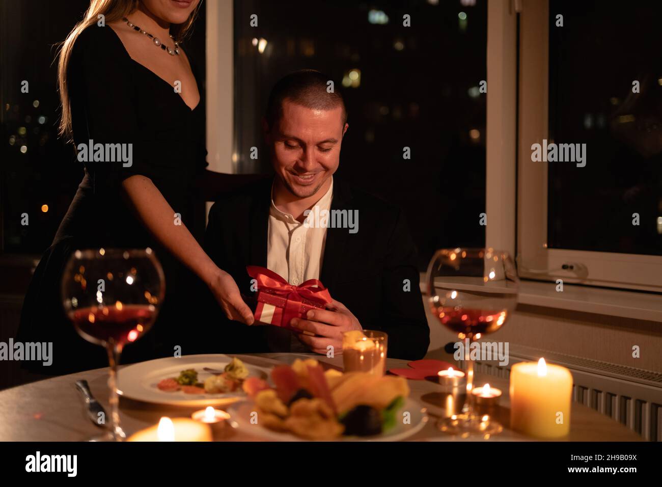 Night date on Valentine's Day, a girl giving a gift to a man dinner with candles, dinner for two, a box with a surprise gift. valentine's celebration Stock Photo