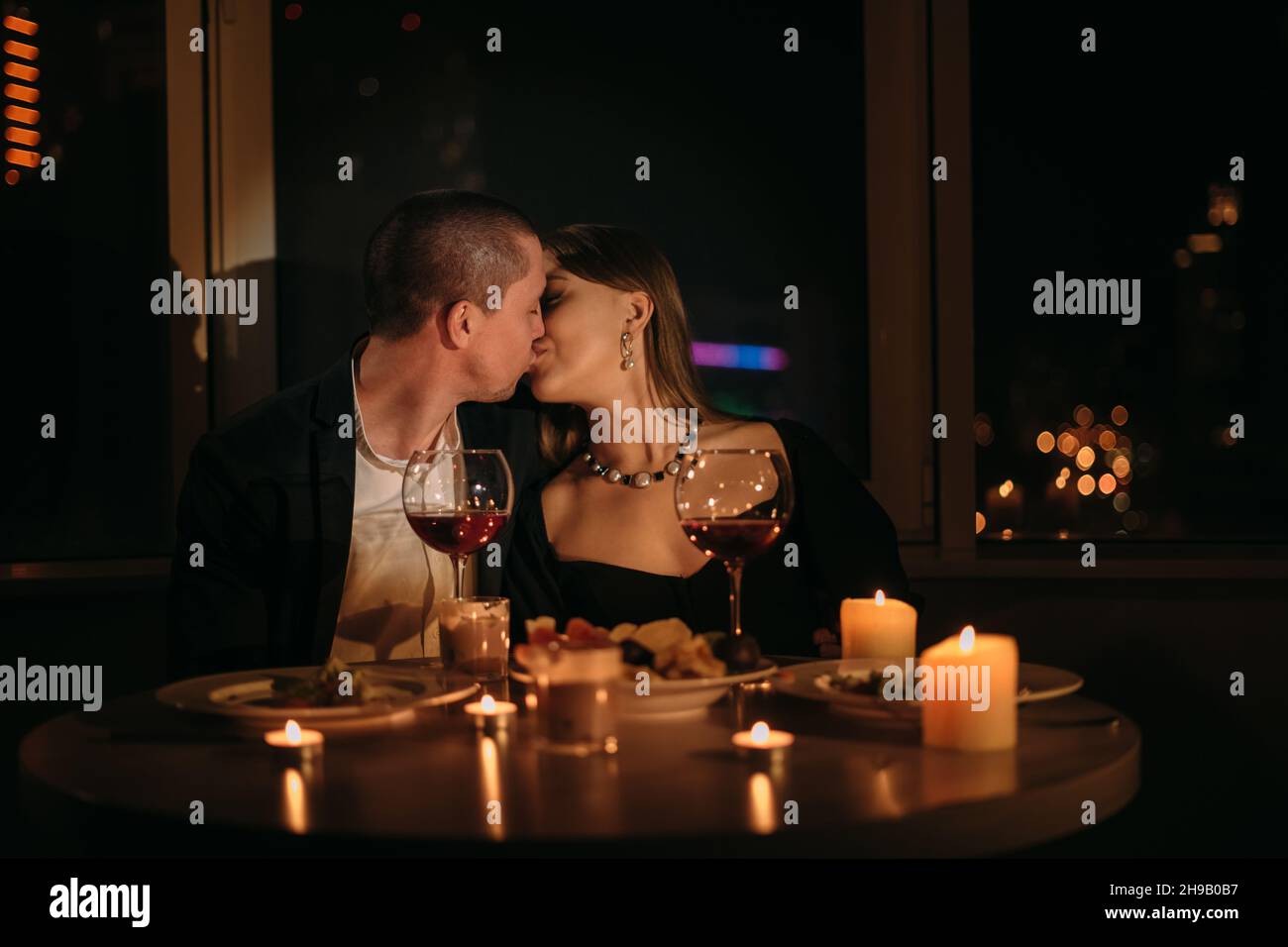 Valentine's day dinner for two, kissing couple at the table, romantic date by candlelight, red wine in glasses for family, man and woman relationship Stock Photo