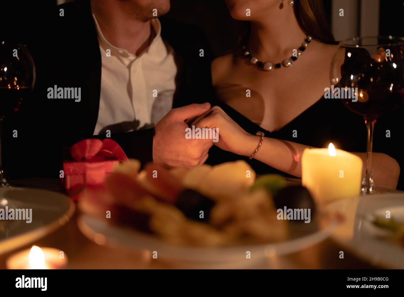 Beautiful passionate couple, romantic candlelight dinner at home, wine in glasses, hold a woman's hand, close-up, Valentine's day celebration Stock Photo