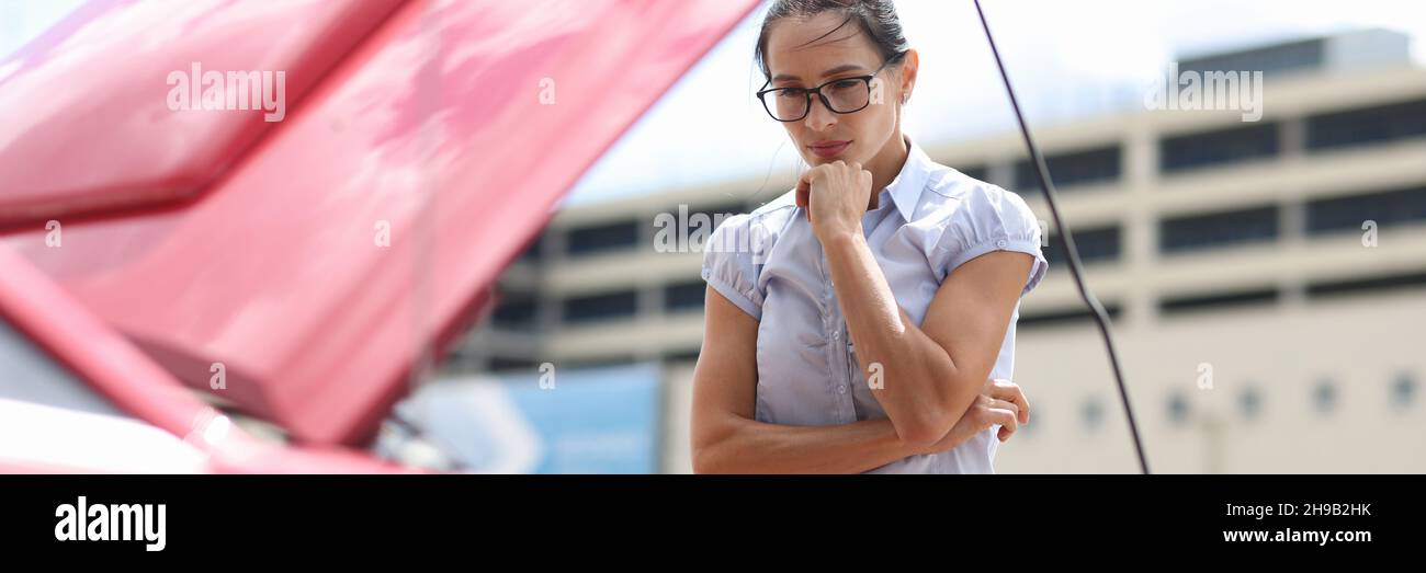 Pensive woman looks at car engine closeup Stock Photo