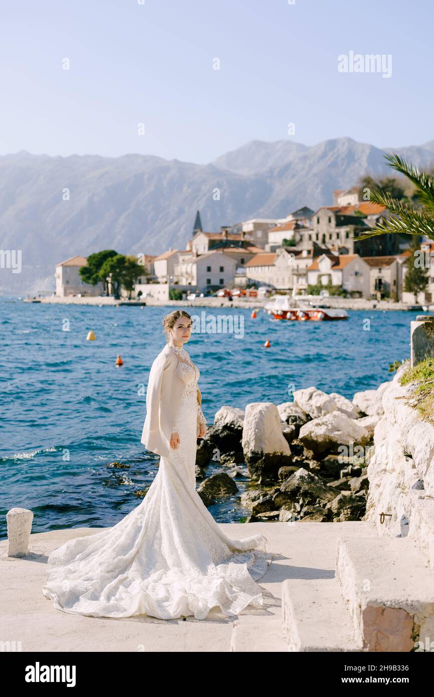 Bride in a long white mermaid dress stands on a pier off the coast of ...