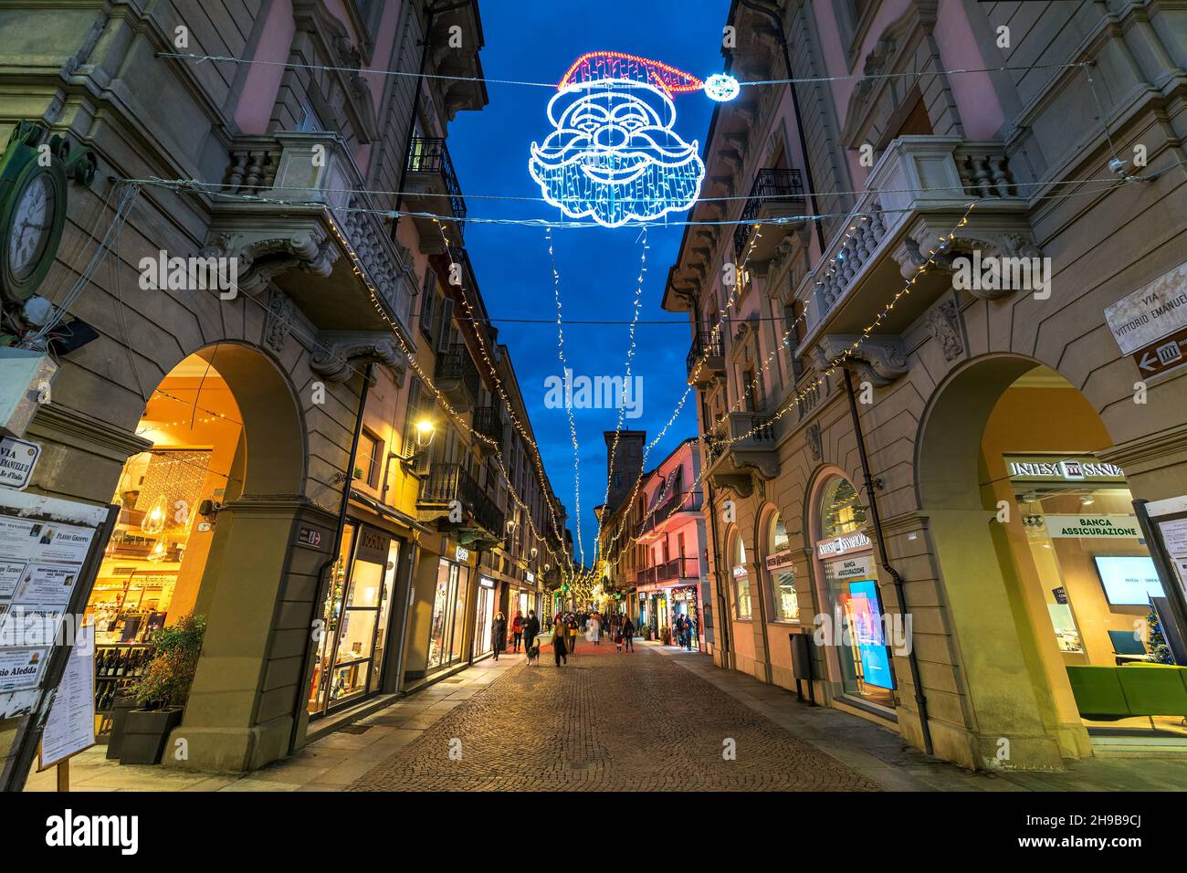 Pedestrian cobblestone street among historic buildings illuminated with Christmas lights in old town of Alba, Italy. Stock Photo