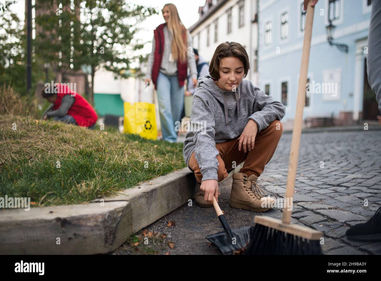 Preteen girl volunteer with team cleaning up street, community service concept Stock Photo