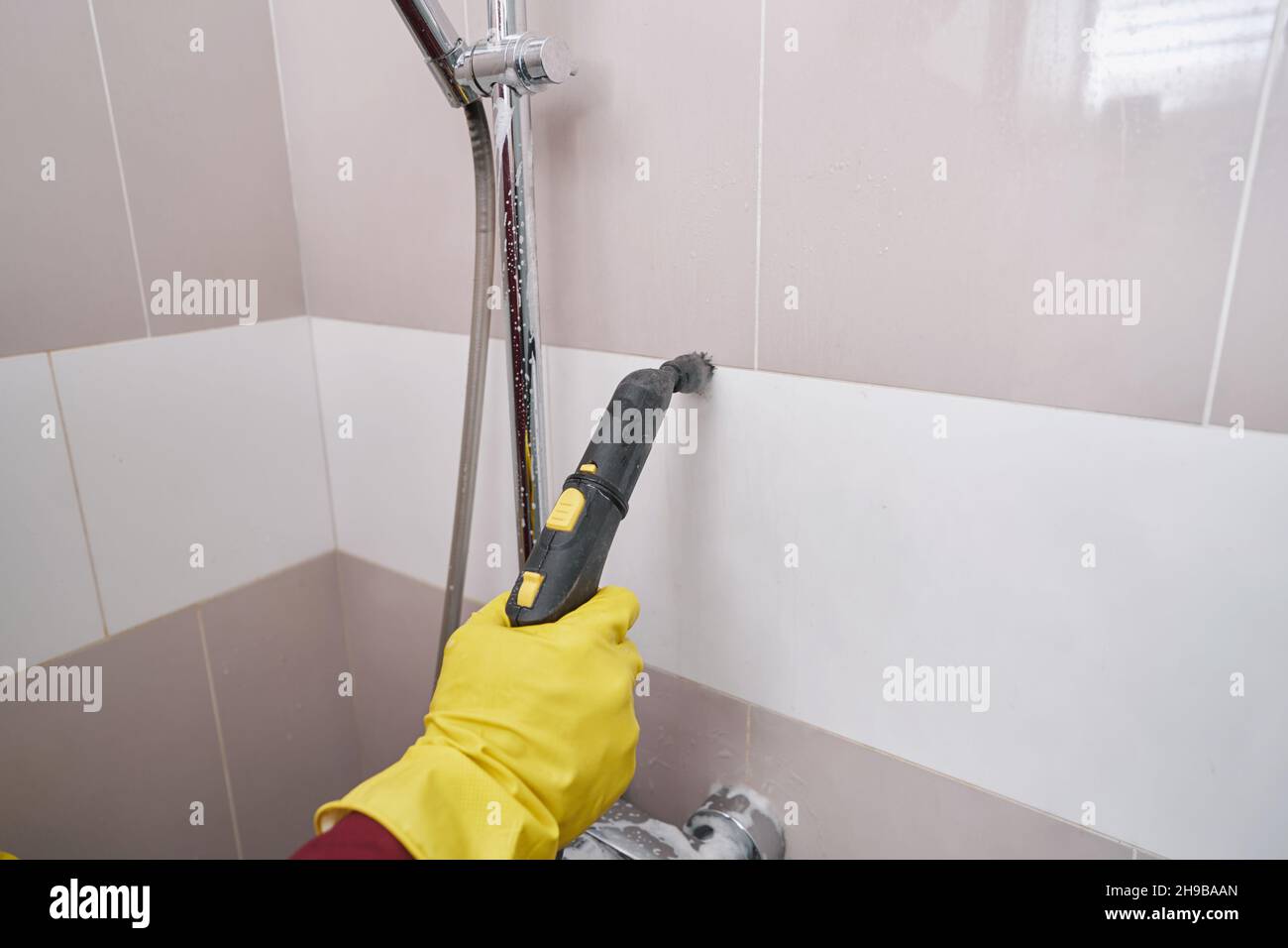 Professional housecleaner steamcleaning grout line on wall Stock Photo