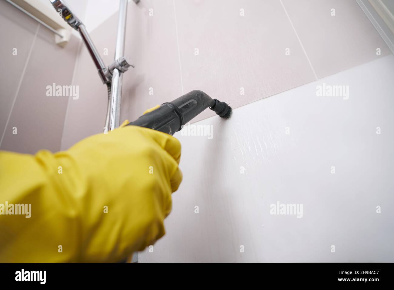 Experienced worker steamcleaning grout line on bathroom wall Stock