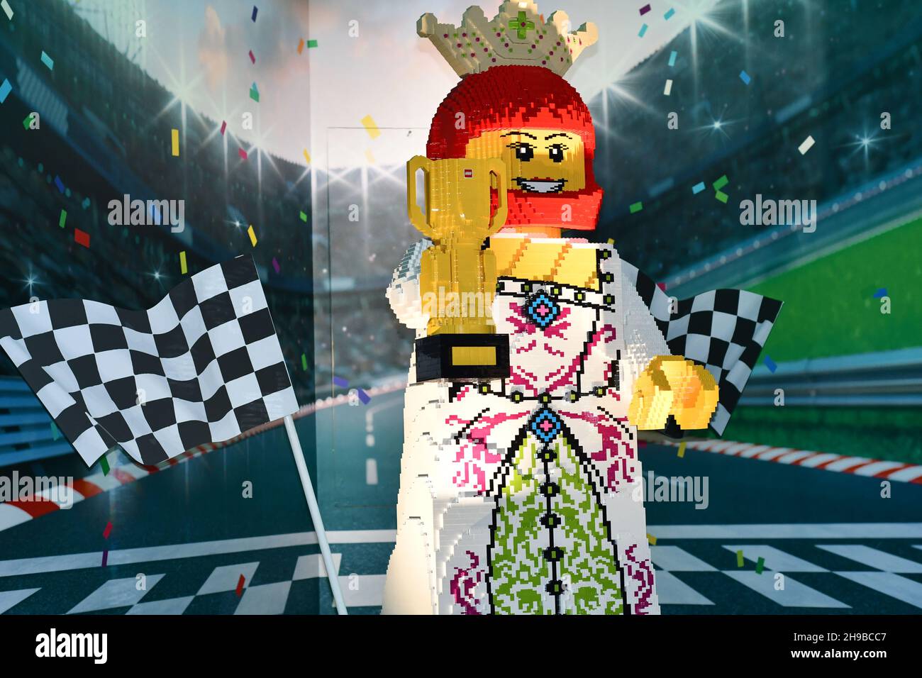 A Lego figure made out of Lego blocks of a racing car driver with a winners trophy with the backdrop of a racing circuit Stock Photo