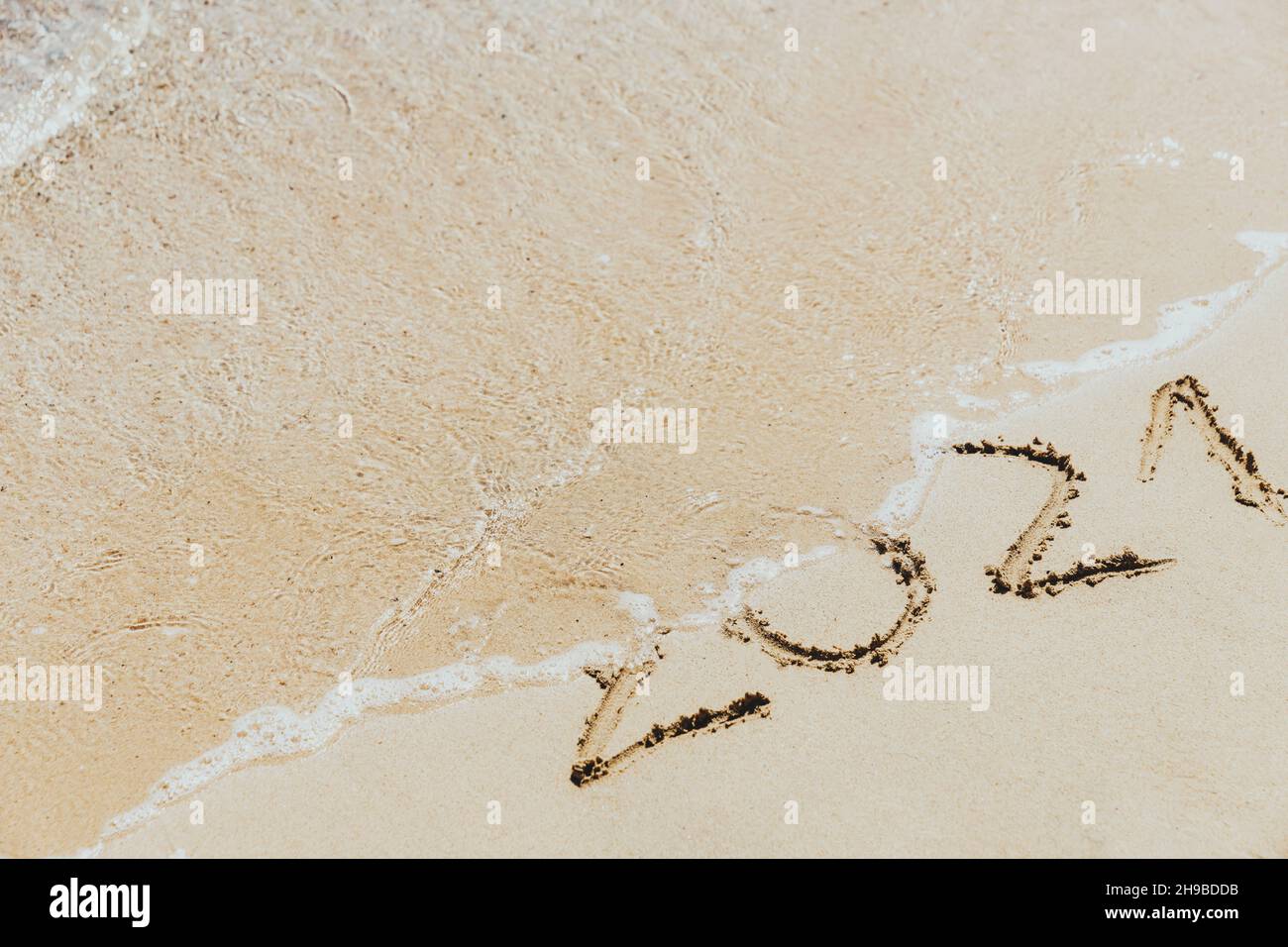 Waves wash away the inscription on the sand 2021. Concept of the outgoing year Stock Photo